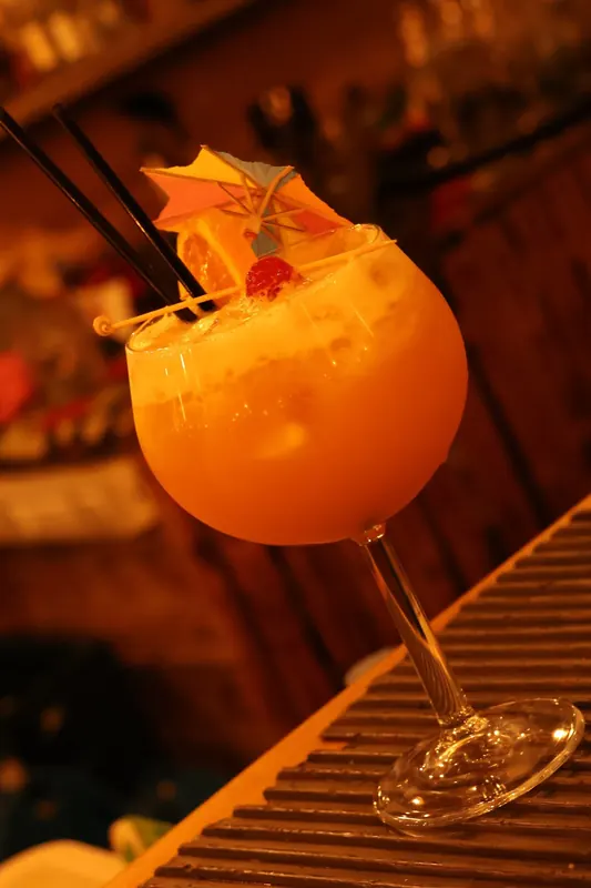 An orange cocktail with a paper umbrella on the bar counter