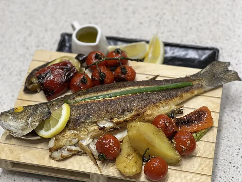 Grilled sea bass on a wooden board with baked potatoes, cherry tomatoes and peppers