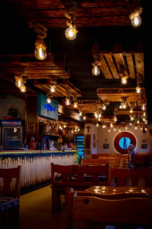 Haxhi's dining room at night: timber pallets on the ceiling, hanging Edison bulbs and a round porthole window