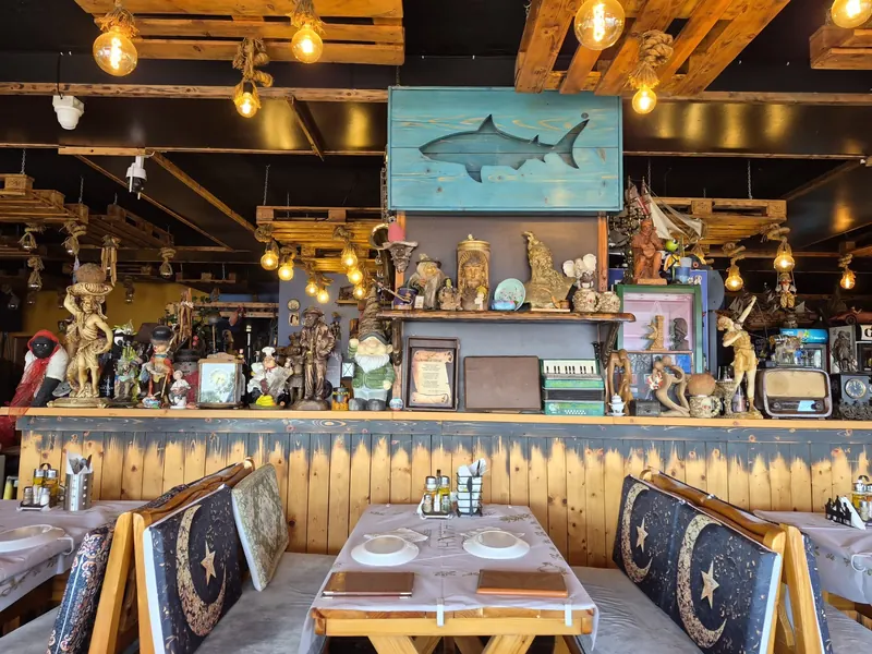The timber bar at Haxhi under hanging Edison bulbs, with a carved shark sign and shelves of curiosities