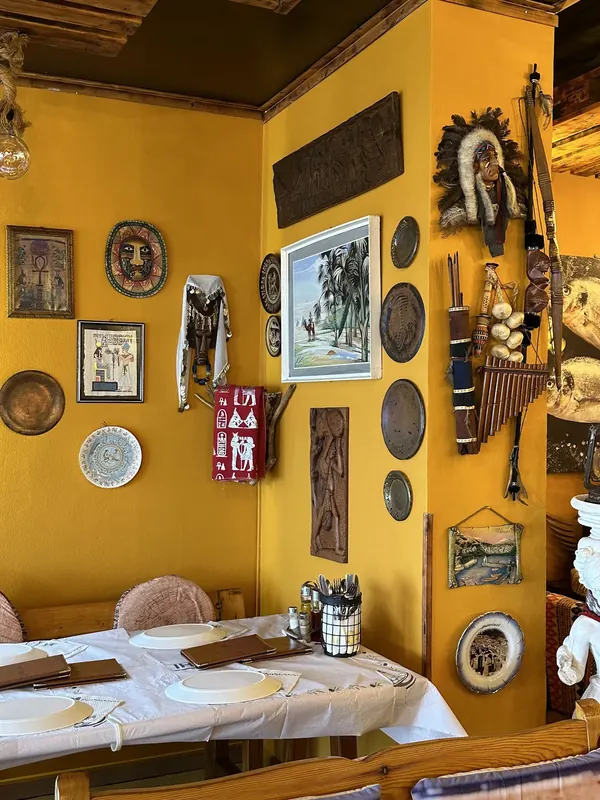 A corner table under a yellow wall hung with plates, masks and paintings