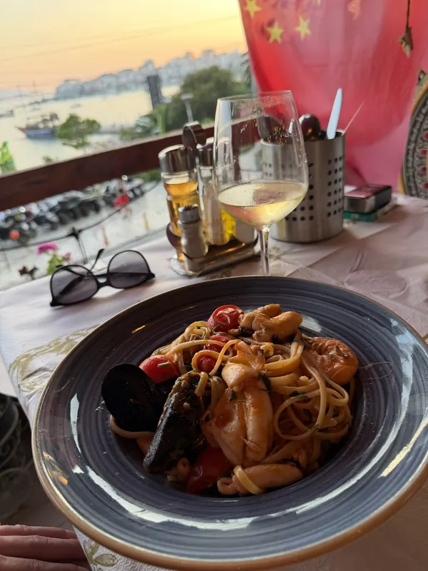 Seafood pasta with mussels, shrimps and calamari, with the Sarandë seafront at sunset behind