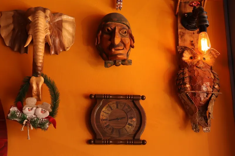 A wall of curiosities at Haxhi: a carved elephant head, a wooden mask, a clock and an owl lamp